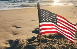 A picture of an American Flag on the Beach during sunrise