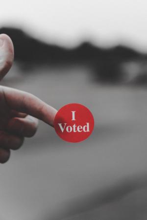 A hand sticking out a finger with a red "I voted" sticker on the finger