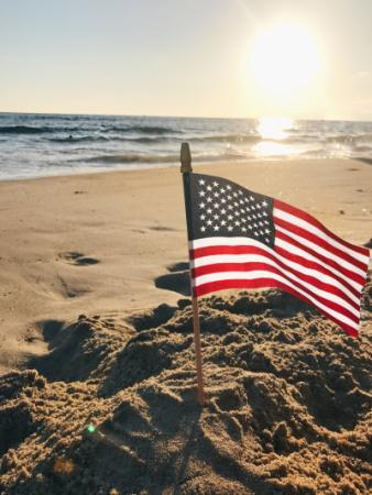A picture of an American Flag on the Beach during sunrise